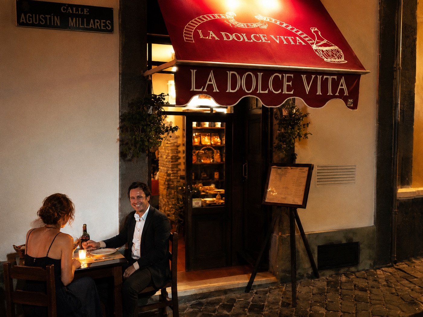 La terraza de La Dolce Vita de noche, una pareja cenando bajo el toldo rojo